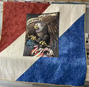 A quilt with diagonal red, white, and blue sections, featuring an image of a bald eagle gripping an American flag and a banner reading These Colors Don’t Run.