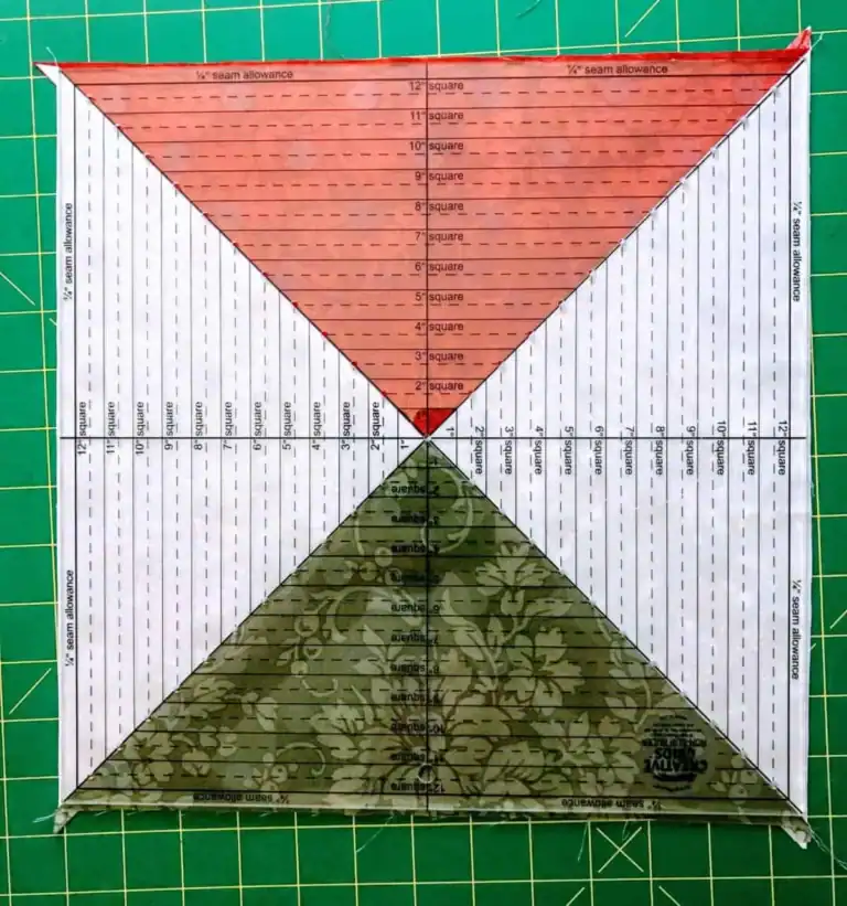 From the Snail Trail Tutorial, this is a square quilting ruler with colored and patterned triangles, divided by diagonal lines, is placed on a green cutting mat. The ruler displays measurement markings and seam allowance guides.