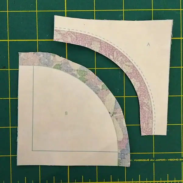Two fabric pieces with paper templates labeled A and B are placed on a green cutting mat with yellow grid lines. Both pieces have curved edges, and sewing guidelines are visible on the templates.